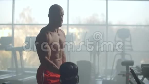 一位运动员在一扇有着美丽身体的窗户的背景下举重来训练你在健身房里的二头肌实力视频的预览图