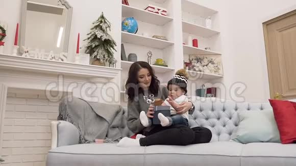 微笑迷人的女人坐在沙发上她的可爱的蹒跚学步的孩子在圣诞节的房间里视频的预览图