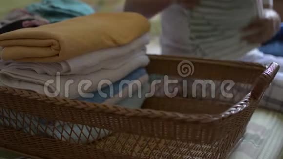女人正在折叠衣服放进一个木篮子里家庭主妇在卧室做家务活视频的预览图