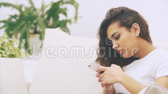 可爱古怪的美国黑人女孩坐在沙发上手里拿着电话发着短信微笑着视频的预览图