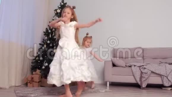 两个穿着漂亮白色连衣裙的女孩姐妹在圣诞树附近跳舞视频的预览图