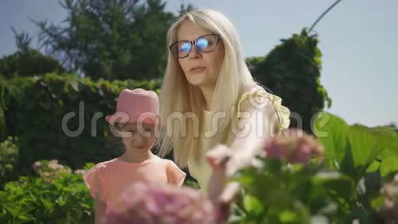 戴眼镜的漂亮妈妈在公园里向她的小女儿展示了一朵盛开的花家庭幸福妇女和女孩视频的预览图