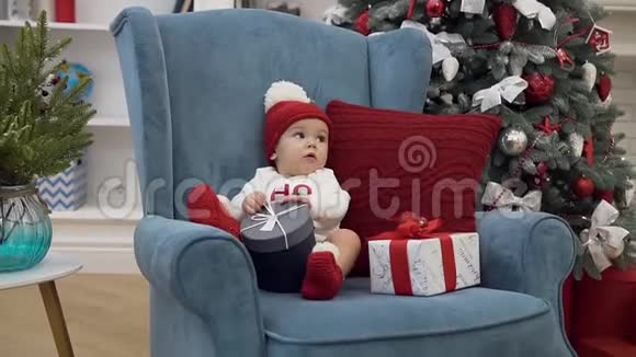 可爱的小女孩穿着圣诞衣服坐在舒适的椅子上坐着新年礼物视频的预览图