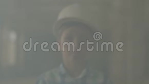 在室内烟雾的背景下戴着保护头盔看着相机的少年肖像火灾概念视频的预览图