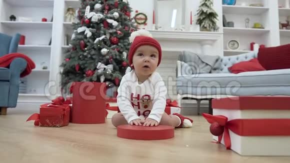 漂亮的小宝宝玩着圣诞盒子的红色盖子坐在中间的木地板上视频的预览图