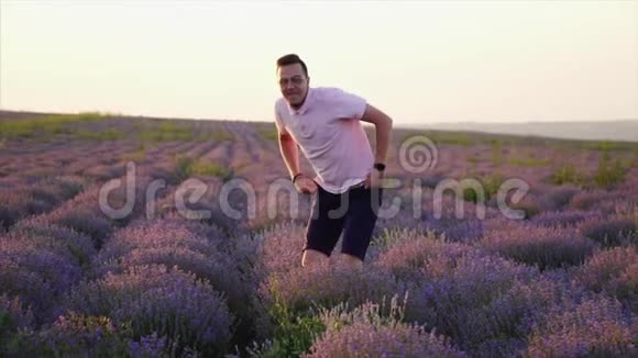 年轻的快乐男人在盛开的薰衣草花田里跳跃慢动作视频的预览图