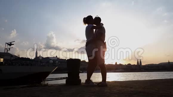 日落时分浪漫情侣在码头拥抱亲吻的剪影视频的预览图