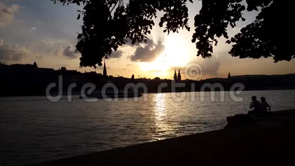 浪漫情侣日落时分在河边码头上与葡萄酒野餐的剪影视频的预览图