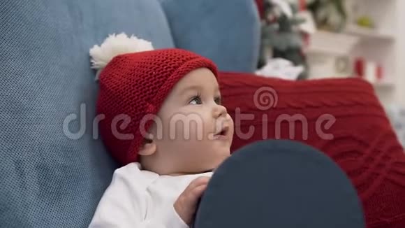 微笑可爱的女婴戴着筒子帽坐在舒适的扶手椅上女性的手摸着她的鼻子视频的预览图