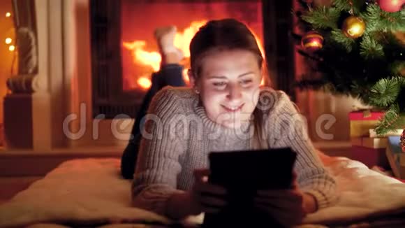 圣诞前夜年轻女子在燃烧的壁炉旁用平板电脑播放4k视频视频的预览图