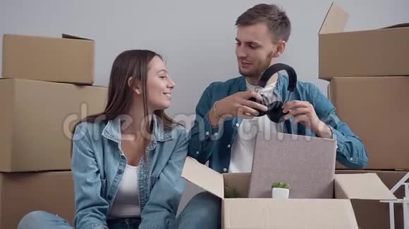 快乐的白种人男子戴着耳机在他的女朋友同时从盒子里拆东西视频的预览图