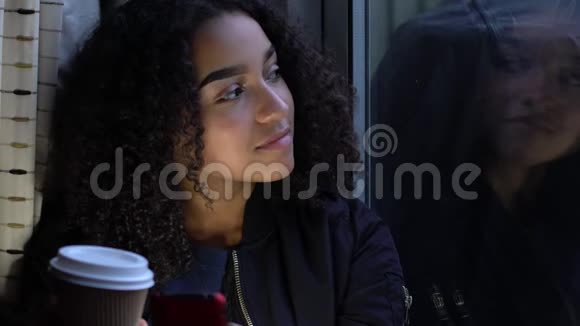 非洲裔美国快乐少女少女少女使用手机望着窗外喝着一杯咖啡视频的预览图