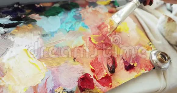 油漆是混合五颜六色的油画颜料在调色板上使用刷子手工特写视频的预览图
