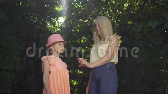 可爱成熟的金发母亲和她漂亮的女儿在夏天的花园或公园里用手指做心形视频的预览图