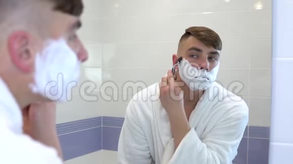 一个年轻人在镜子前剃头一个穿着白大褂脸上有泡沫的人剃了头发视图视频的预览图
