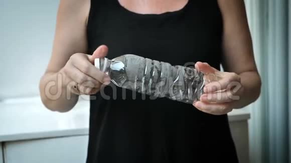一个女人压缩一个塑料瓶来回收它视频的预览图