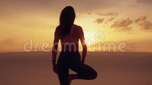 沙漠中一条腿上站立的女性冥想瑜伽平衡剪影视频的预览图
