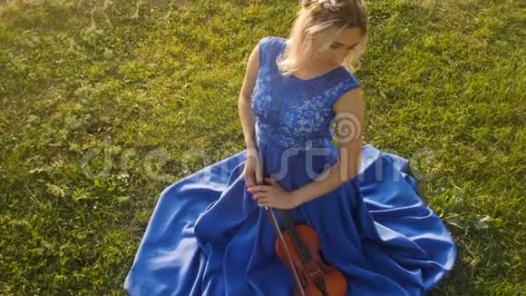 年轻美丽的女人在大自然中拉小提琴女孩坐在绿草上穿着一件长裙子拿着乐器自负视频的预览图