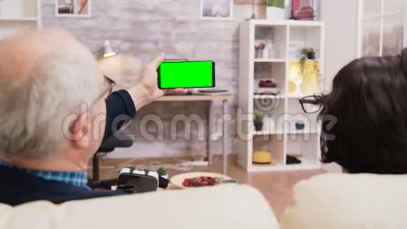 老年夫妇观看绿色屏幕手机的后视图视频的预览图