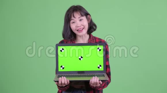 快乐的亚洲时髦女人一边说一边展示笔记本电脑视频的预览图