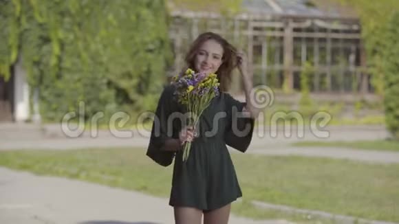 肖像嬉戏的年轻女子手持一束野花站在户外看着相机概念视频的预览图