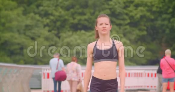 近距离正面观看年轻漂亮的运动女性慢跑者在桥上行走的肖像背景是视频的预览图