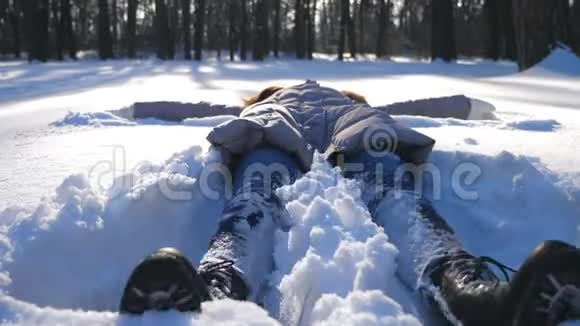穿着冬装的小女孩躺在雪地草地上做天使快乐的女人在雪地里玩享受冬天的时光视频的预览图