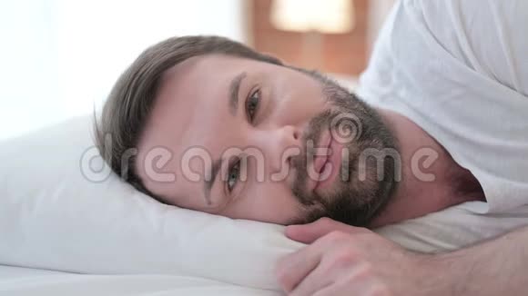 在床上相机微笑的快乐胡子年轻人视频的预览图