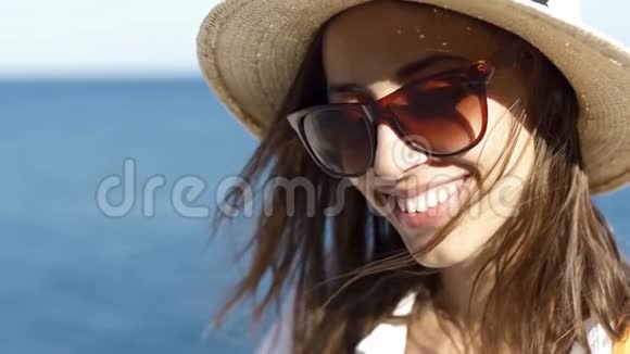 美丽的微笑女旅行者带着草帽和太阳镜在海边放松站在阳光明媚的蓝海上视频的预览图