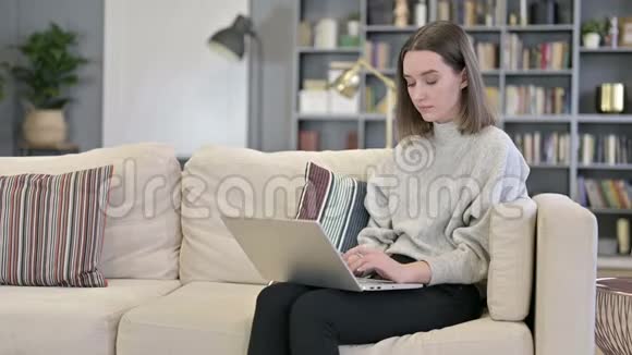雄心勃勃的年轻女子在沙发上的笔记本电脑上工作视频的预览图