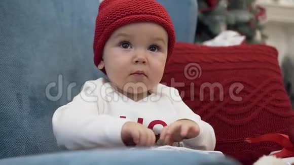 贴心可爱的蹒跚学步的孩子戴着筒状帽子坐在舒适的扶手椅上抱着枕头玩着圣诞节视频的预览图