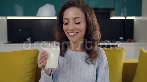 一位年轻漂亮的女士喝着一杯牛奶坐在厨房里舒适的沙发上视频的预览图