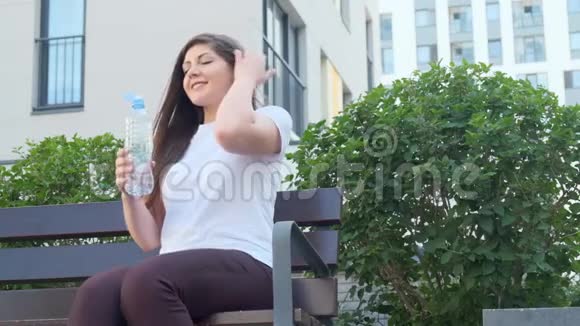 一个年轻的女人坐在城市的长椅上喝水视频的预览图