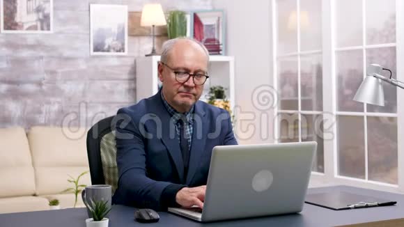 在笔记本电脑上工作的老人喝了一口咖啡视频的预览图