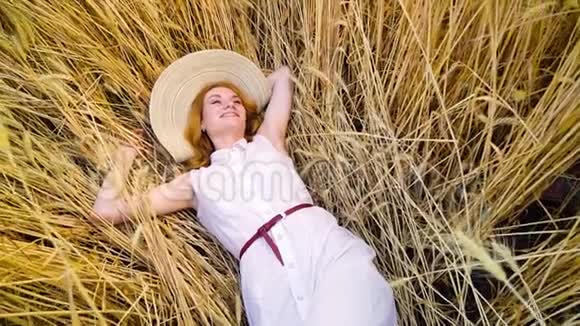 摄像机拍摄着躺在麦田里休息的年轻红头发女人视频的预览图