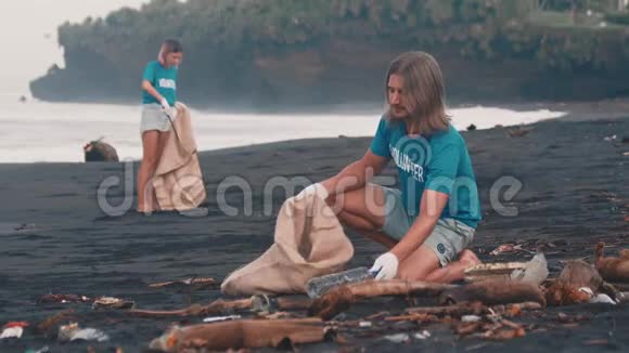 志愿者穿着蓝色t恤清理海滩上的垃圾把垃圾叠在生态袋里视频的预览图