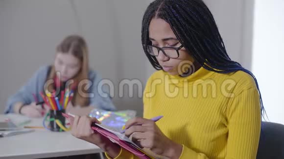 聪明的非裔美国女孩在笔记本上写作修眼镜看相机微笑自信的学生视频的预览图