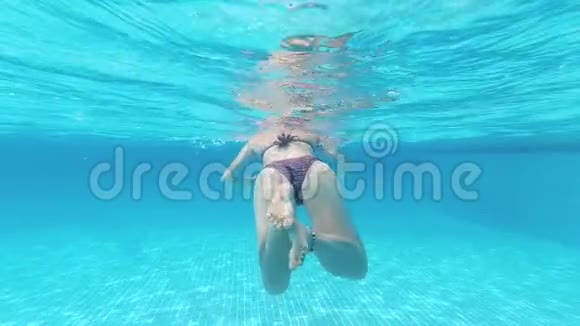 年轻女子在清澈的蓝色泳池水中水下游泳的后景慢镜头视频的预览图