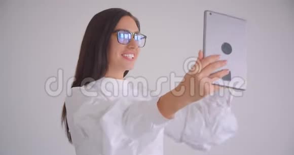 戴着眼镜的年轻漂亮的白种人女商人的特写肖像在平板电脑上播放视频兴高采烈地交谈视频的预览图