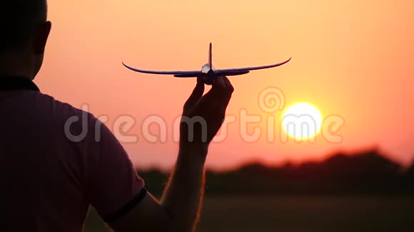 一个男人手里拿着一架模型飞机的剪影在日落时站在太阳面前旅游概念视频的预览图
