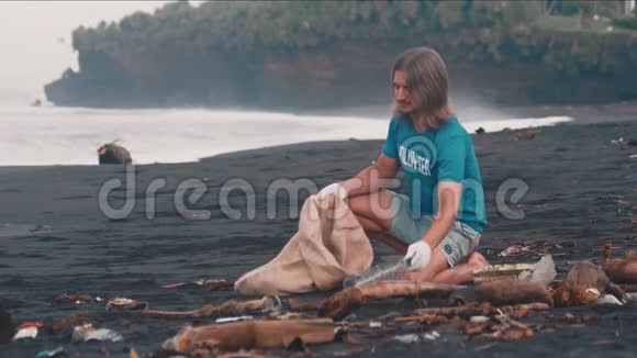 志愿者穿着蓝色t恤清理海滩上的垃圾把垃圾叠在生态袋里视频的预览图