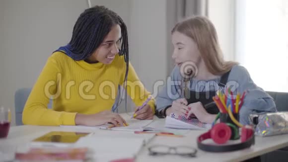 积极的高加索女孩与非裔美国女性朋友交谈快乐的学生在室内做作业学习视频的预览图