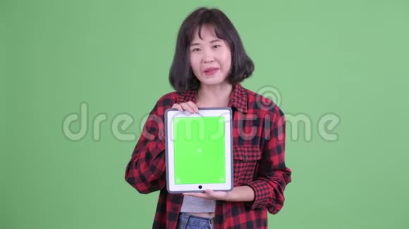 快乐的亚洲时髦女人一边说一边展示数字平板电脑视频的预览图