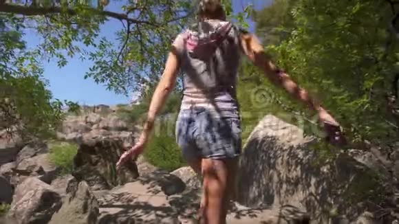 穿着牛仔裤短裤和凉鞋的苗条女人在森林里的石头间散步视频的预览图