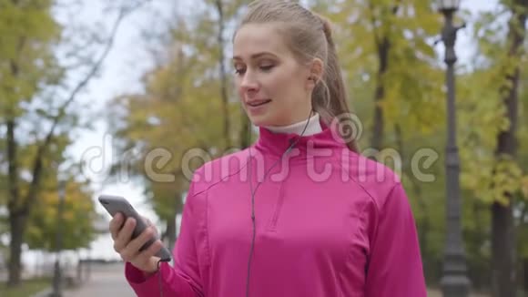 年轻的高加索女人穿着粉红色运动服耳机里打开音乐开始跑步女运动员培训视频的预览图