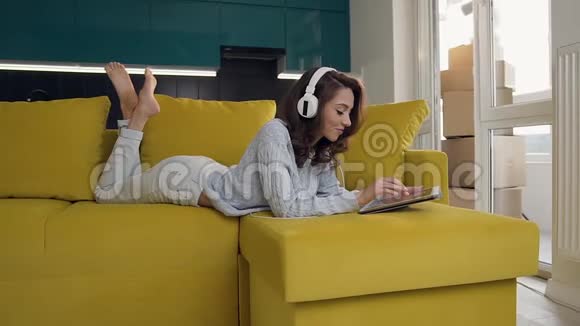 带着耳机听着ipad音乐在舒适的沙发上放松的年轻女士笑容愉快视频的预览图