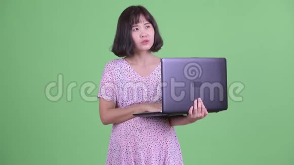 快乐的亚洲孕妇用笔记本电脑思考视频的预览图