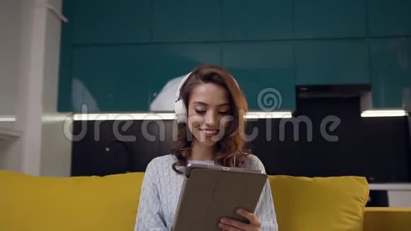 一个30岁的女孩带着笔记本电脑手里拿着耳机听着厨房背景下的音乐视频的预览图