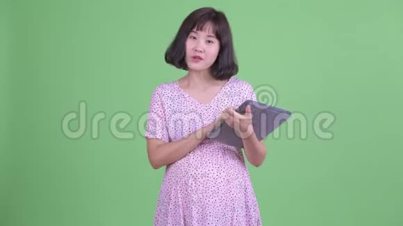 快乐的亚洲孕妇用数码平板电脑说话视频的预览图