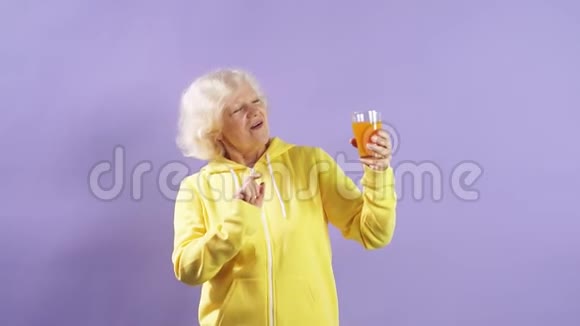 穿着黄色毛衣的快乐老太太跳舞喝新鲜胡萝卜汁视频的预览图